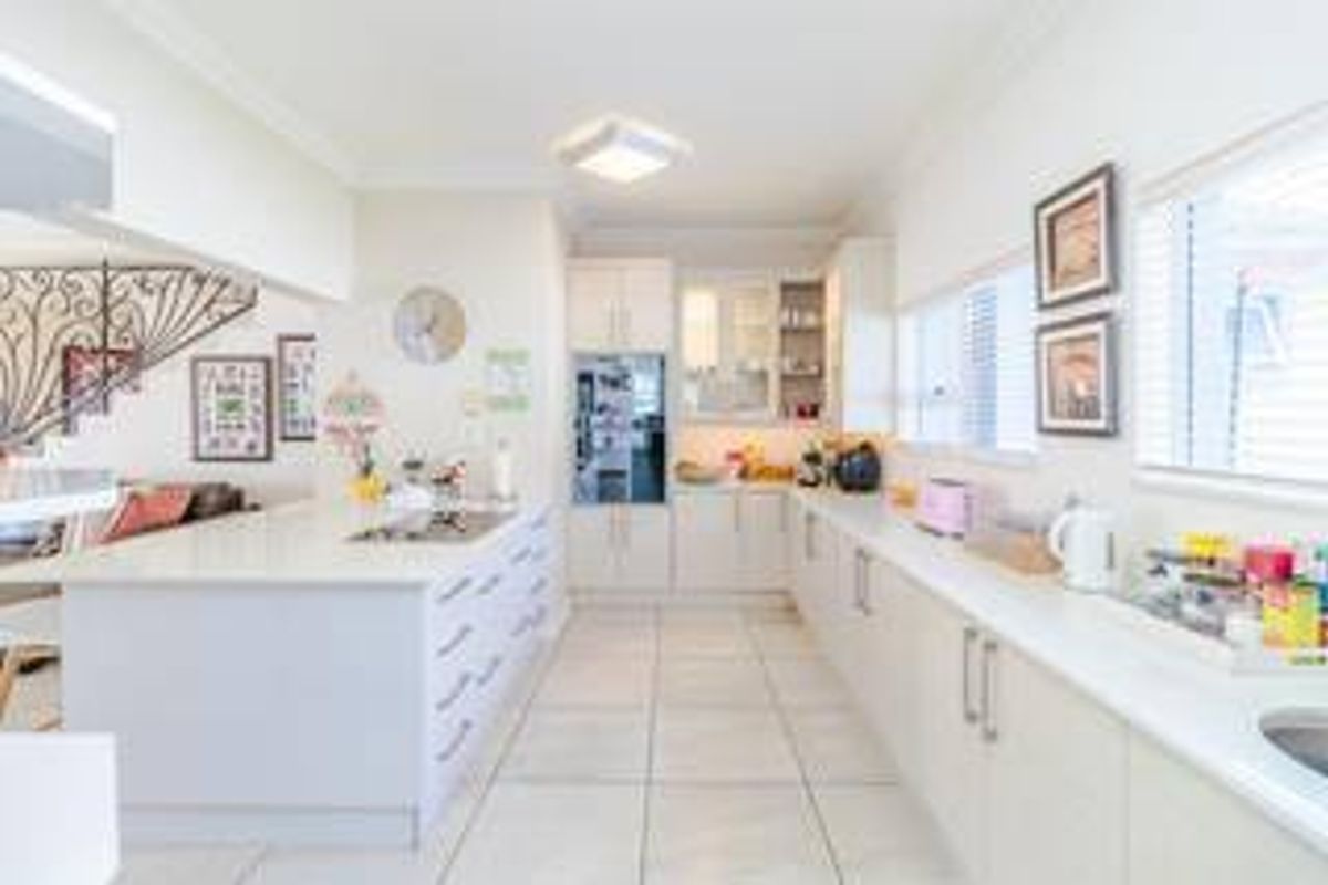 Modern kitchen featuring a large central island, stone countertops, built-in oven, and ample cabinetry, finished with neutral tiled flooring and recessed lighting.