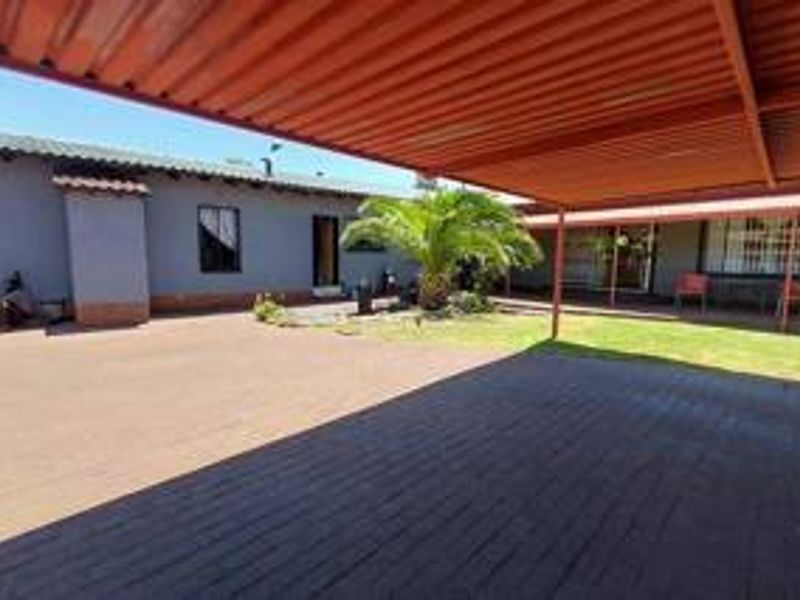 A spacious rear courtyard featuring a large covered patio area, paved flooring, and a well-maintained lawn with established garden greenery.