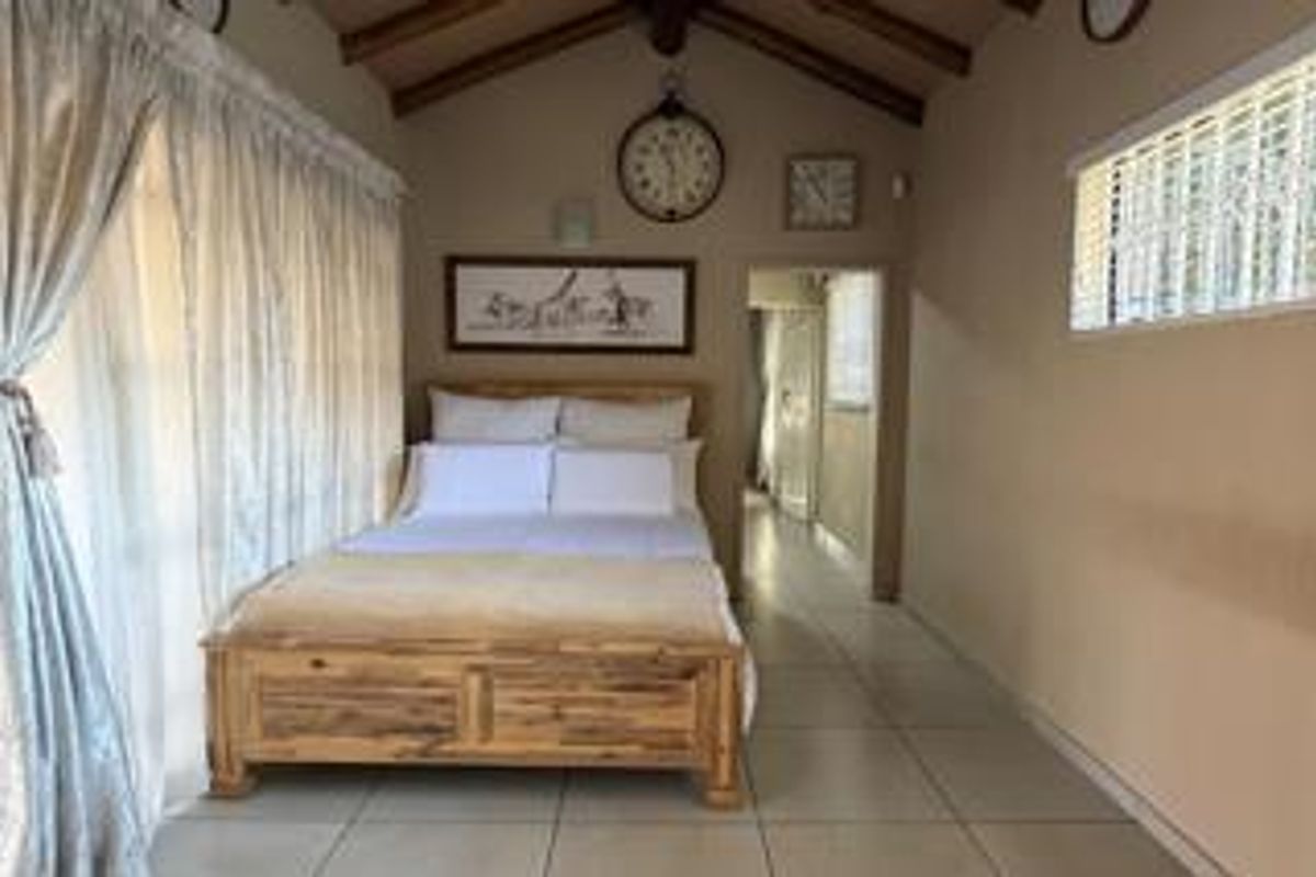 A bedroom featuring exposed timber ceiling beams, tiled flooring, and a sliding glass door providing natural light.