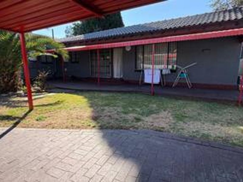 Rear view of the property featuring a covered patio area, paved driveway, and a small garden space with established landscaping.