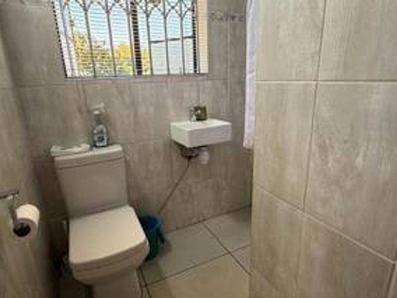 Compact bathroom featuring tiled walls and flooring, a wall-mounted basin, and a standard toilet with security bars on the window.
