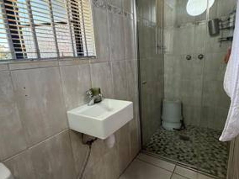 A functional bathroom featuring a wall-mounted basin, a walk-in shower with a pebble tile floor, and neutral wall tiling.