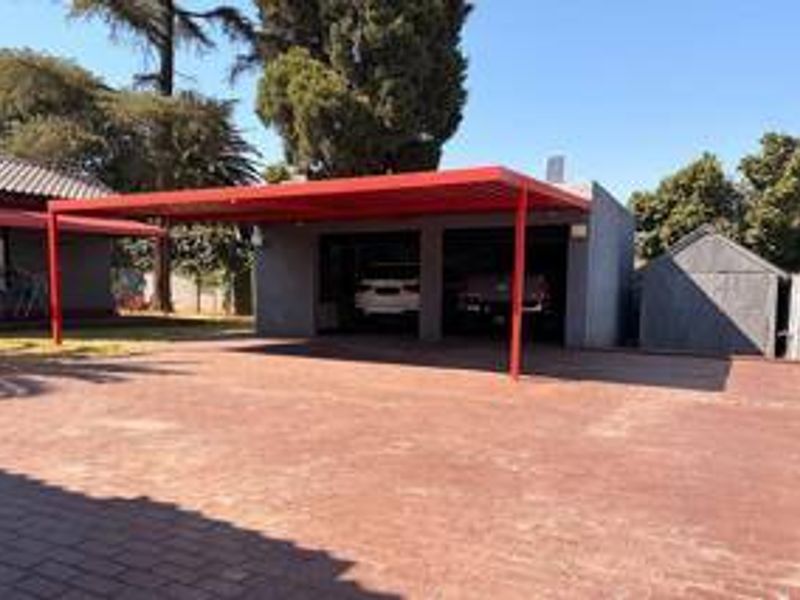 A double garage with an attached red metal carport and a spacious paved driveway, providing ample off-street parking.