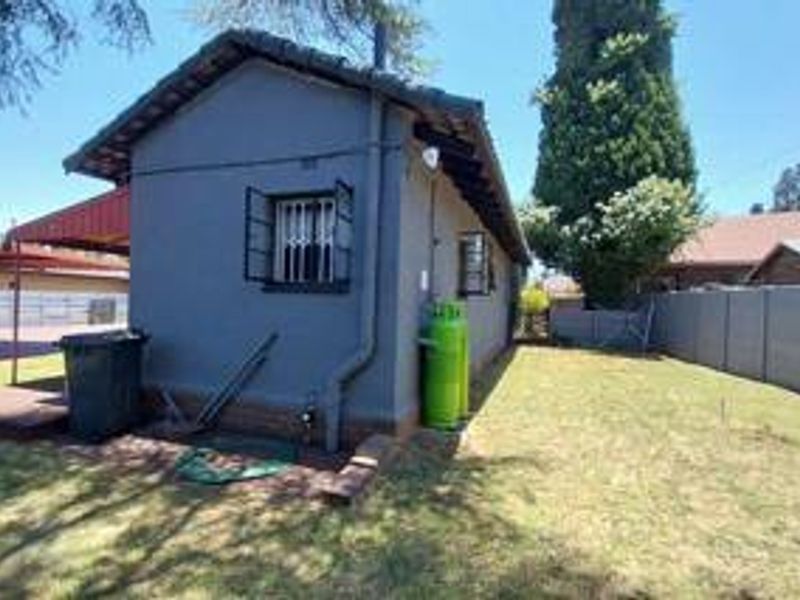 Rear view of the property featuring a tiled roof, security bars on windows, and a fenced garden area with a precast concrete boundary wall.