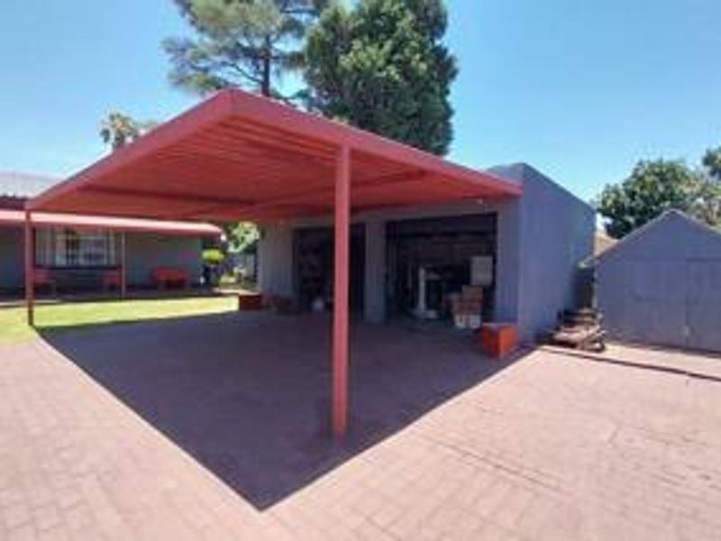 Rear exterior view featuring a paved driveway, a covered carport, a double garage, and a detached storage shed in the backyard.