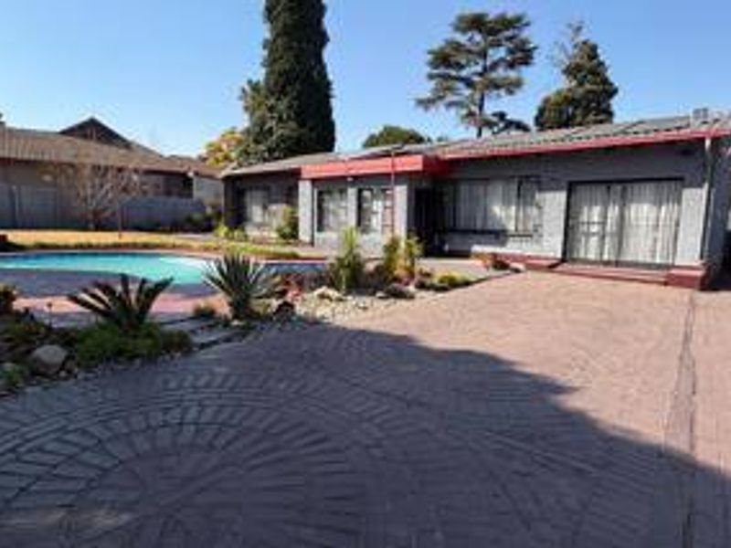 Rear view of the property featuring a swimming pool, extensive paved area, and sliding glass doors leading into the home.