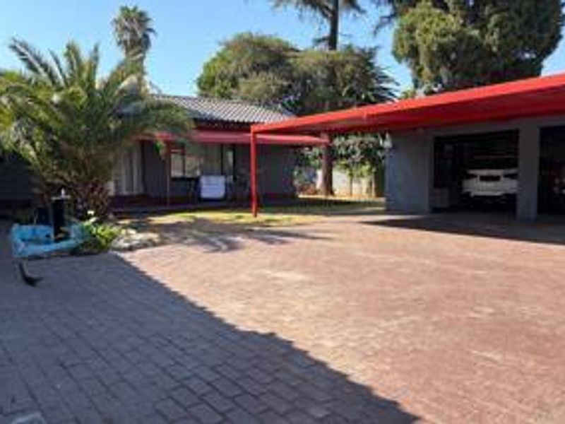 Front view of the property featuring a spacious paved driveway and a double carport with a red roof structure.