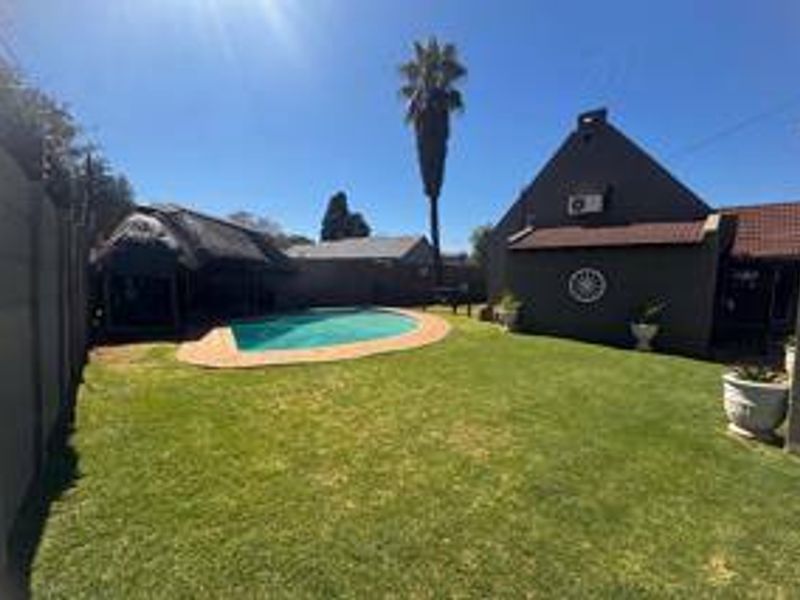 A private backyard featuring a swimming pool, a thatched lapa entertainment area, and a well-maintained lawn enclosed by perimeter walls.