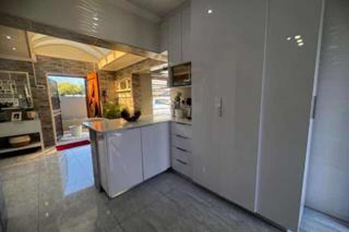 Modern kitchen featuring high-gloss cabinetry, stone countertops, built-in microwave, and sleek tiled flooring, with an open flow to the adjacent living area.