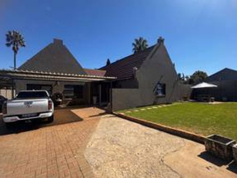 Front exterior view of the property featuring a paved driveway, carport, and a well-maintained lawn area.