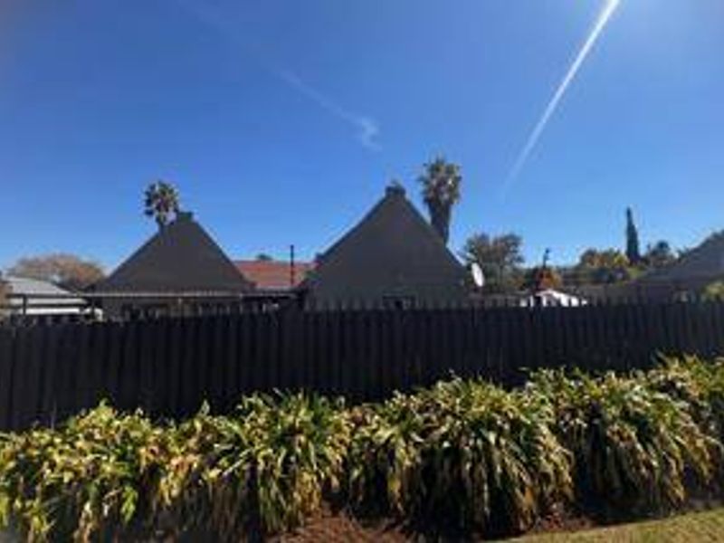 Rear view of the property featuring a pitched roof structure, enclosed by perimeter fencing and established garden landscaping.