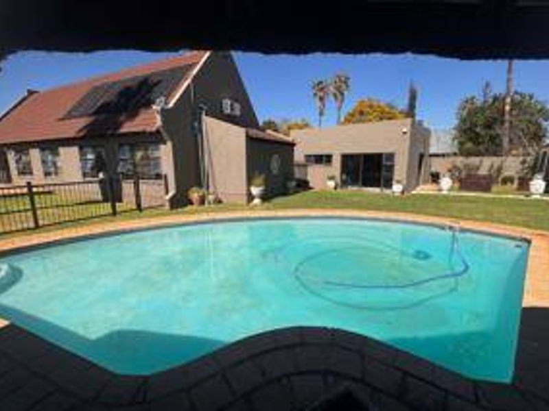 A well-maintained backyard featuring a swimming pool with solar heating panels, surrounded by a paved deck and a neat lawn area.