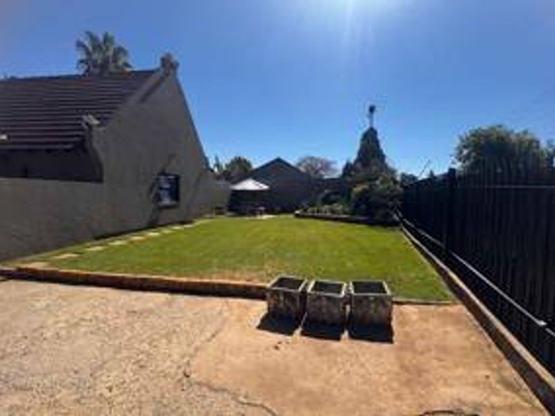 A rear exterior view featuring a private lawn, concrete driveway, and secure metal perimeter fencing.