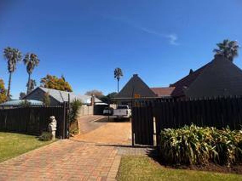Front view of the property featuring a paved driveway, secure perimeter fencing, and gated entrance leading to the main residence.