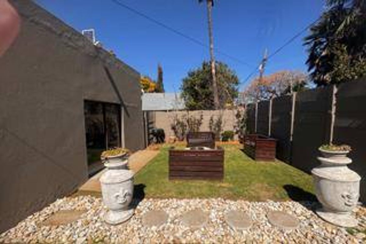 A private rear garden area featuring a small lawn, gravel pathway, and sliding door access to the main dwelling.
