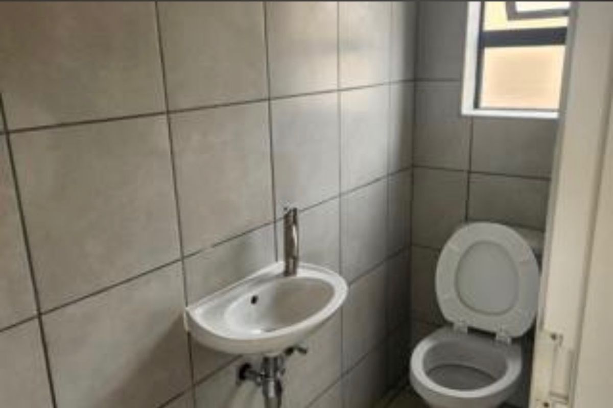 A compact guest bathroom featuring neutral ceramic wall tiles, a wall-mounted basin with chrome fixtures, and a standard toilet.