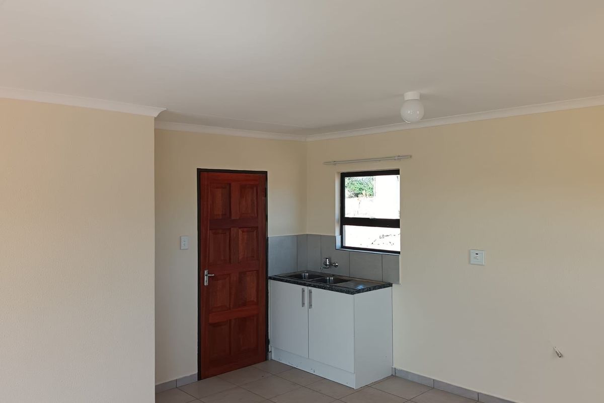 A compact, empty kitchen area featuring a single base cabinet with a sink, tiled flooring, and a timber door.