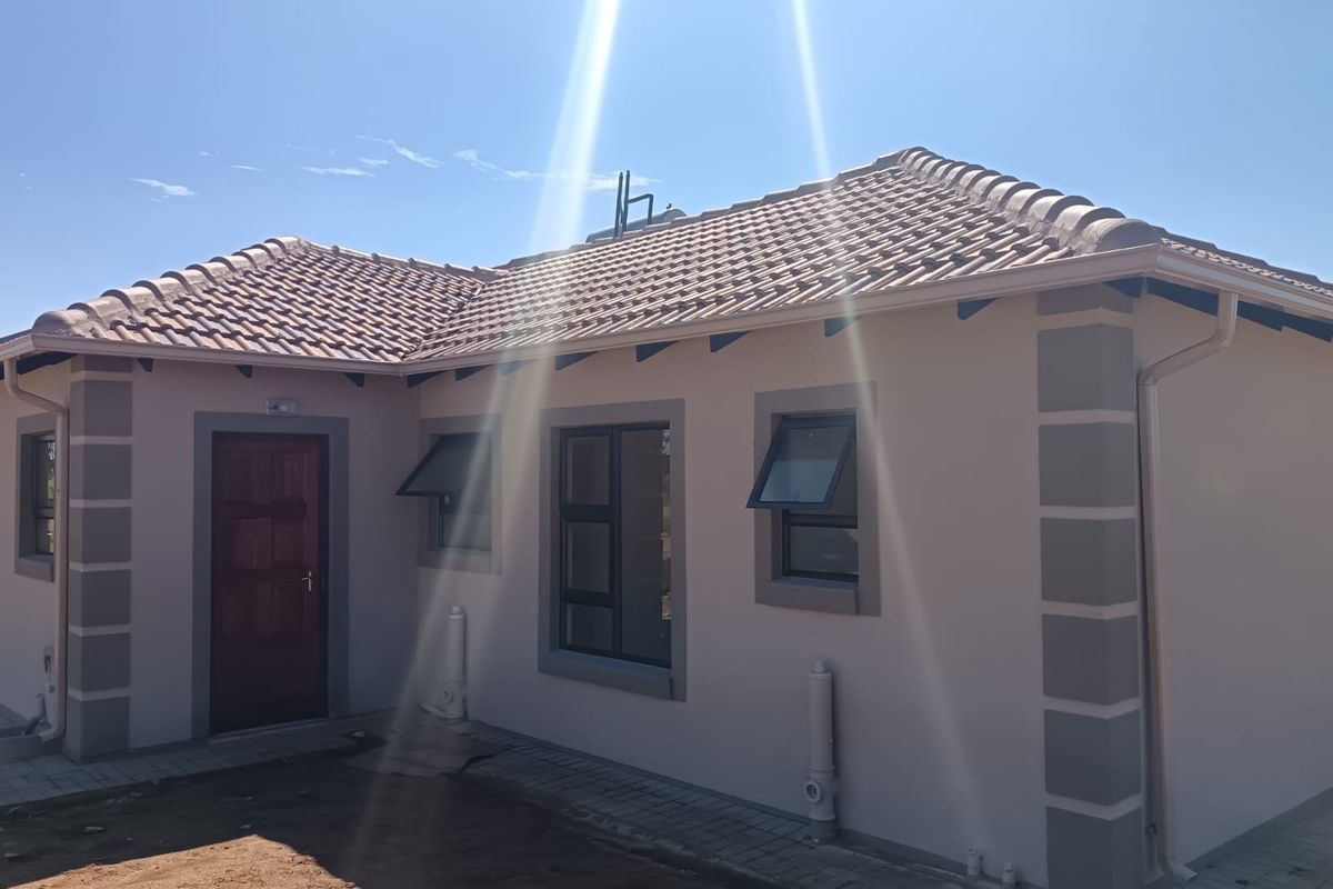 A well-maintained rear exterior view of the house featuring a tiled roof, modern aluminium window frames, and paved walkways.