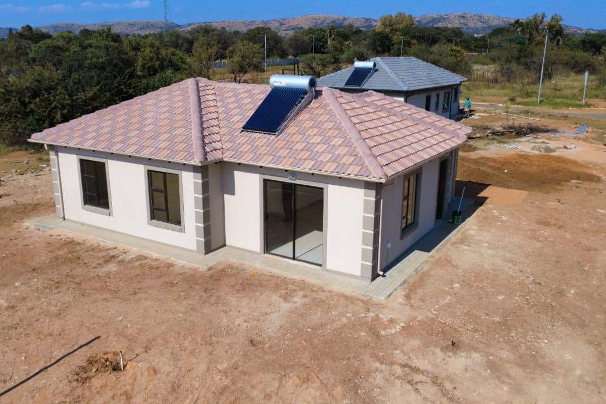 Aerial view of a modern single-story house featuring a tiled roof with solar water heating and surrounding unlandscaped grounds.