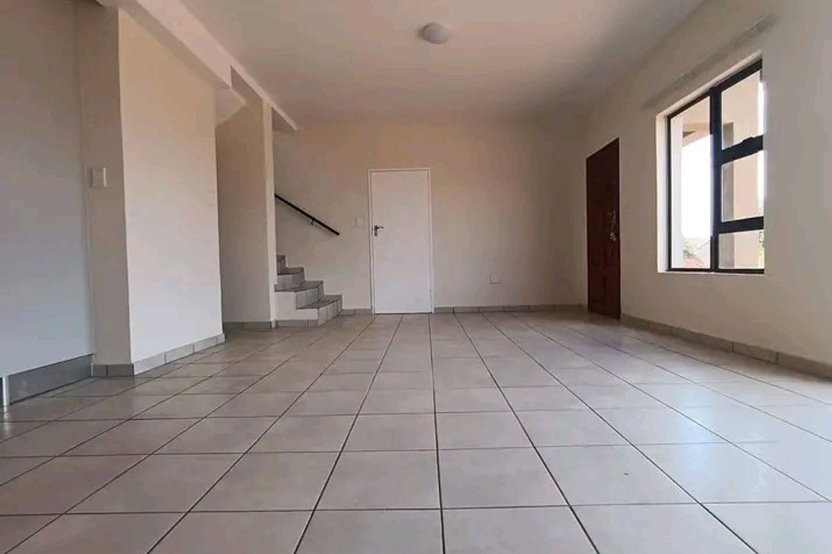 An open-plan living area featuring neutral tiled flooring, a staircase, and large windows providing natural light.