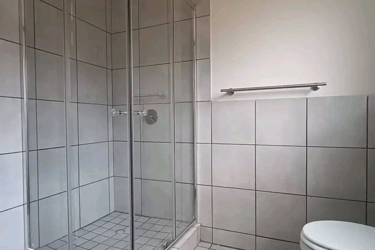 A clean, functional bathroom featuring a glass-enclosed shower, tiled walls and flooring, and standard sanitary fixtures.