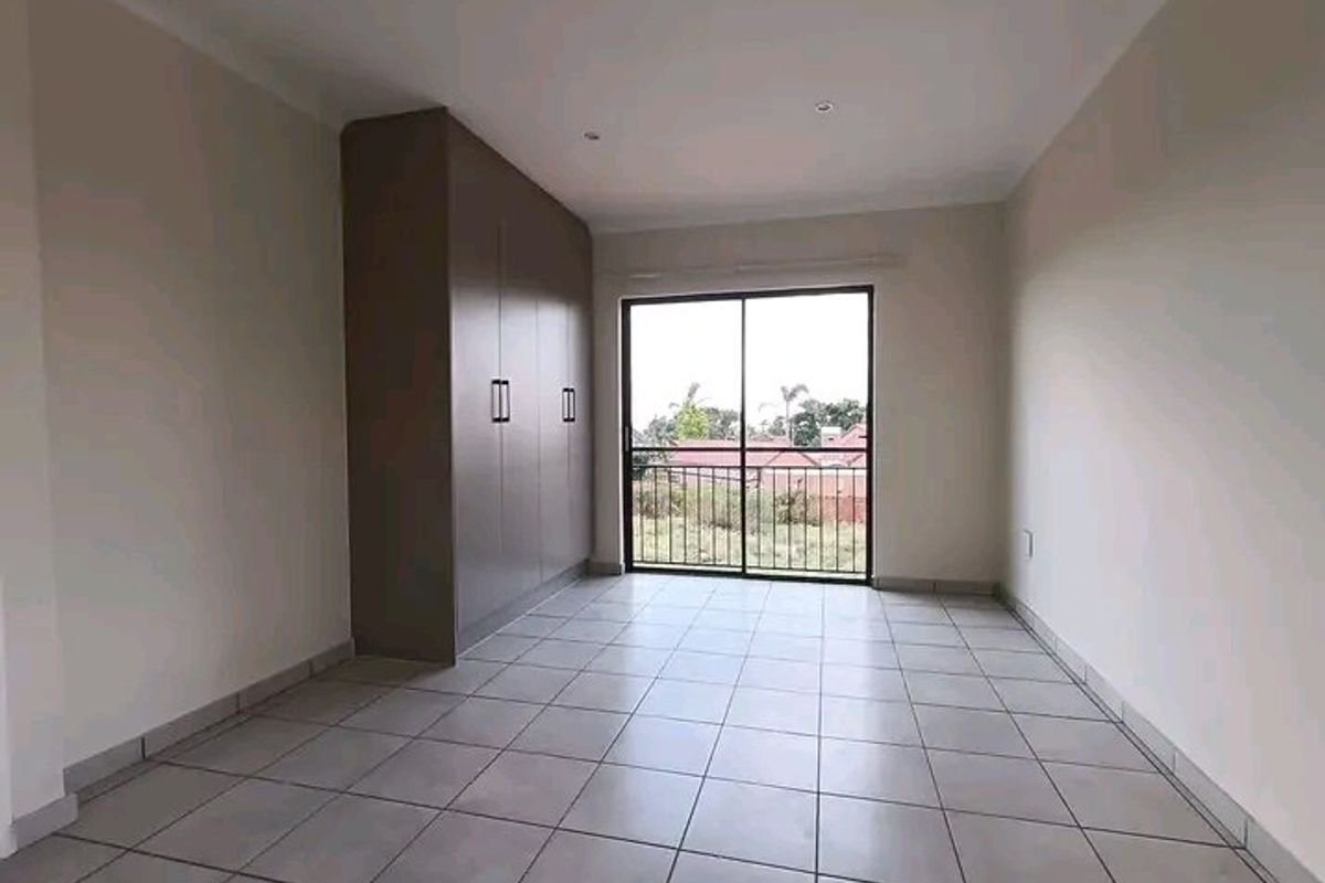 A bright, empty bedroom featuring neutral tiled flooring, built-in cupboards, and a sliding glass door leading to an outdoor view.