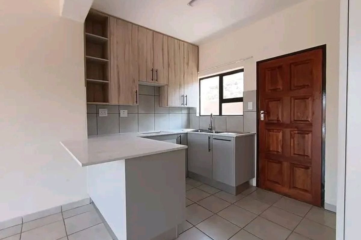 A clean, modern kitchen featuring light wood-tone cabinetry, stone countertops, tiled flooring, and a functional layout with a breakfast bar.