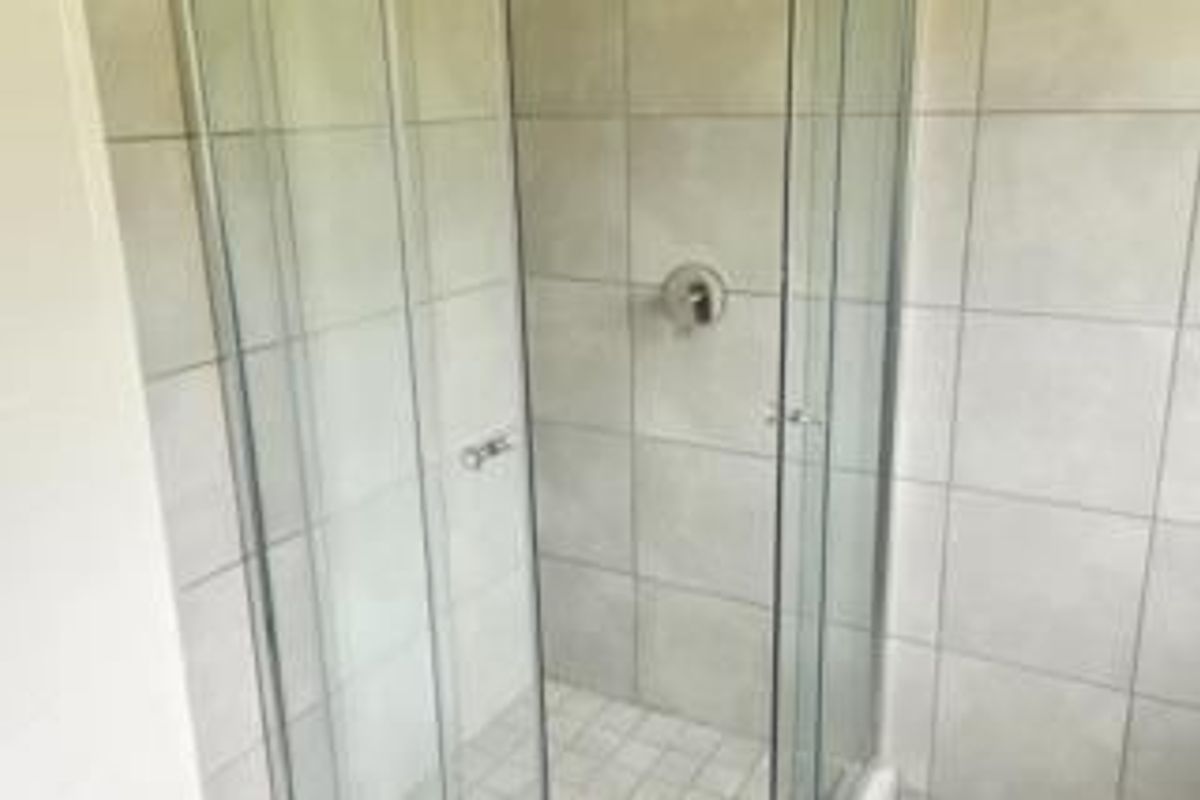 A clean, modern bathroom shower enclosure featuring neutral wall tiles and a glass door.