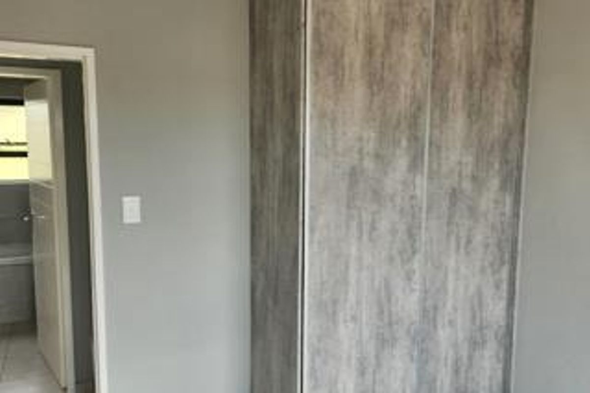 A bedroom interior featuring a modern wood-look built-in wardrobe and a doorway leading to an adjacent room.