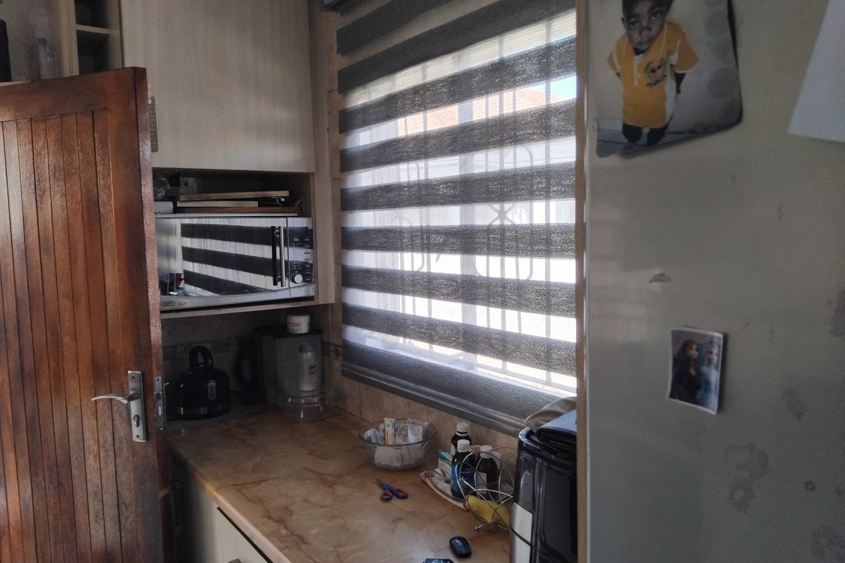 A compact kitchen area featuring built-in cabinetry, a laminate countertop, and a built-in microwave, with natural light provided by a window with roller blinds.