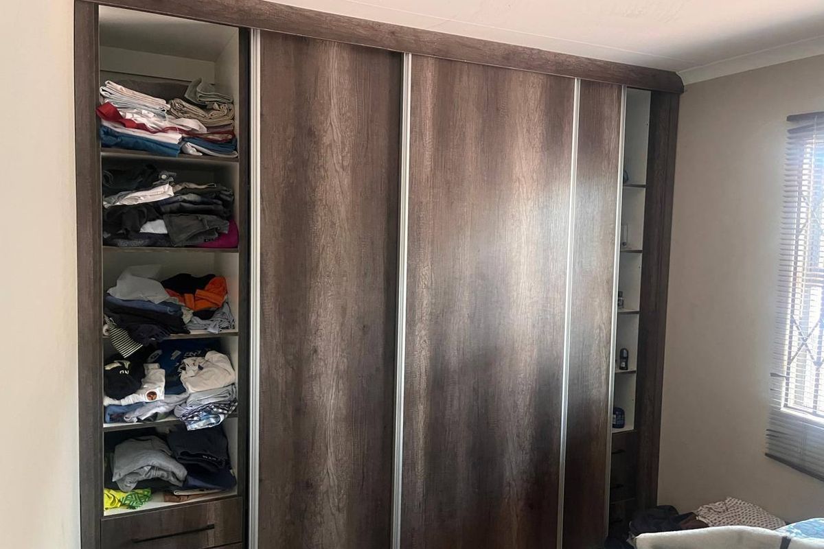 A bedroom featuring a large, dark wood-finish built-in wardrobe with sliding doors and integrated shelving.
