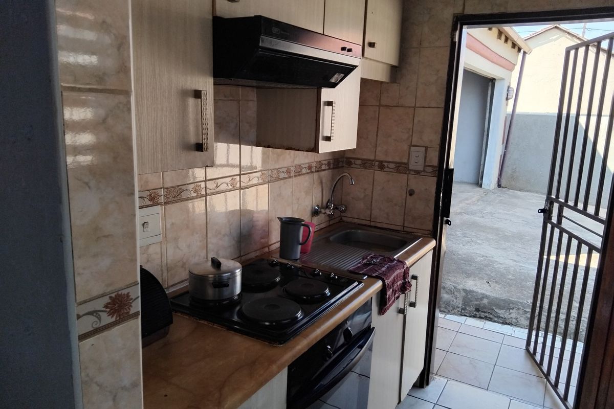 Compact kitchen featuring built-in cabinetry, electric hob, oven, extractor fan, and stainless steel sink, with direct access to the exterior via a security gate.