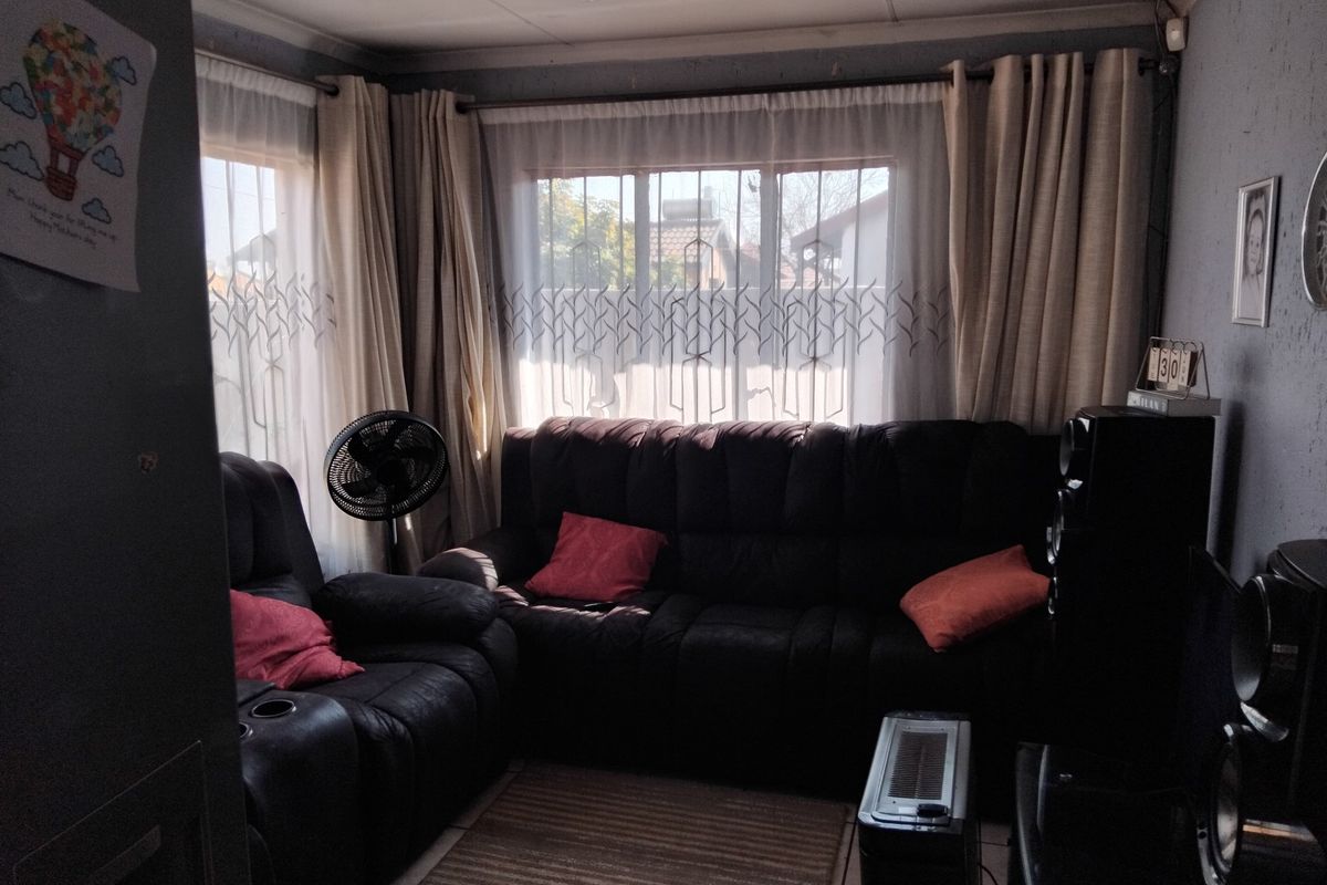 A cozy living room featuring tiled flooring and large windows with curtain rails, providing natural light to the space.