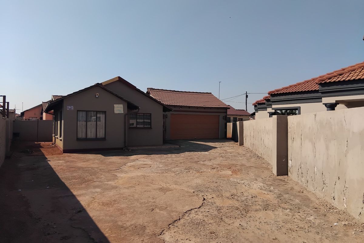 Rear view of the property featuring a detached garage, tiled roof, and a large, unpaved driveway area enclosed by perimeter walls.