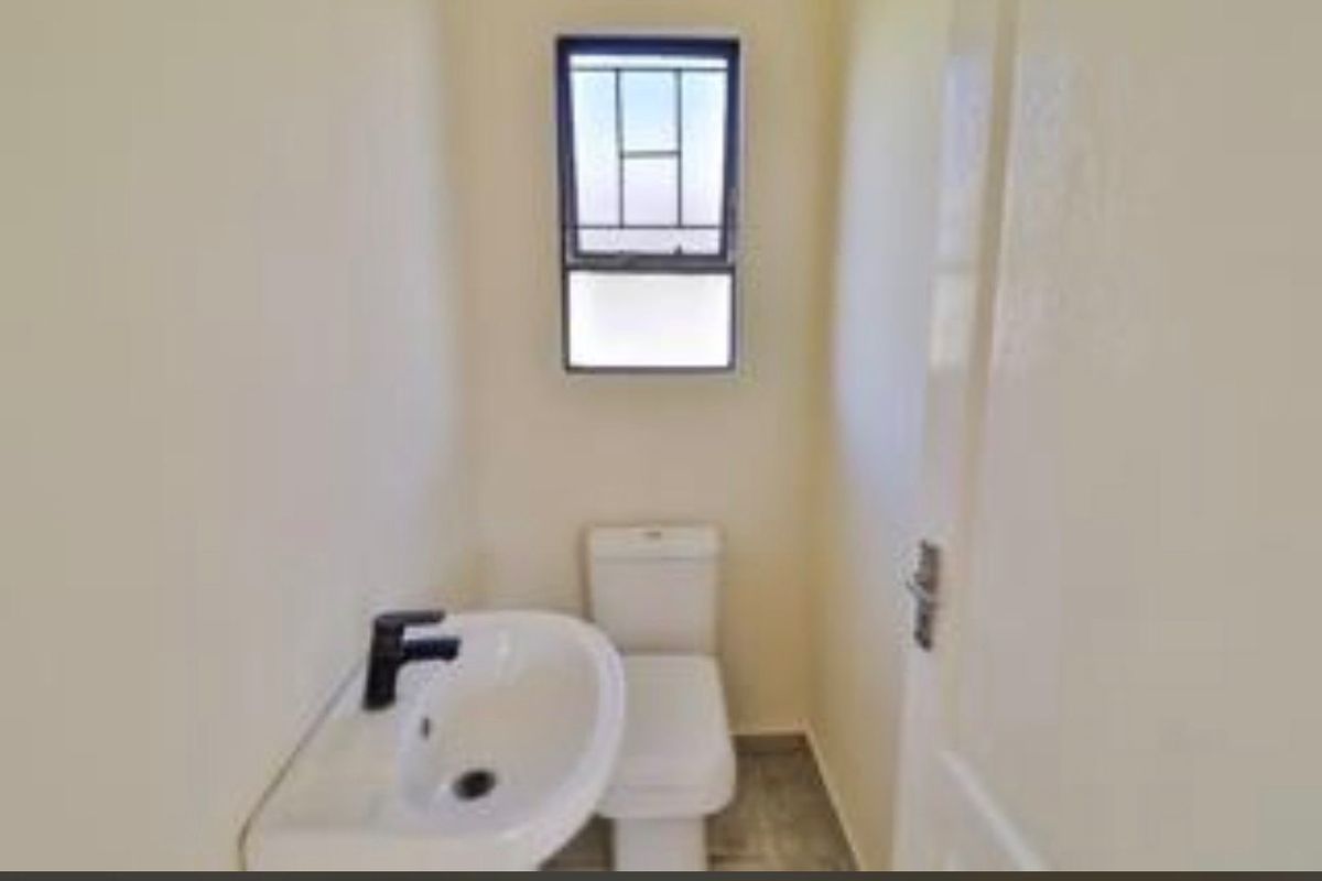 A clean and functional guest bathroom featuring a modern white toilet, a wall-mounted washbasin with a black faucet, and a window with security bars.