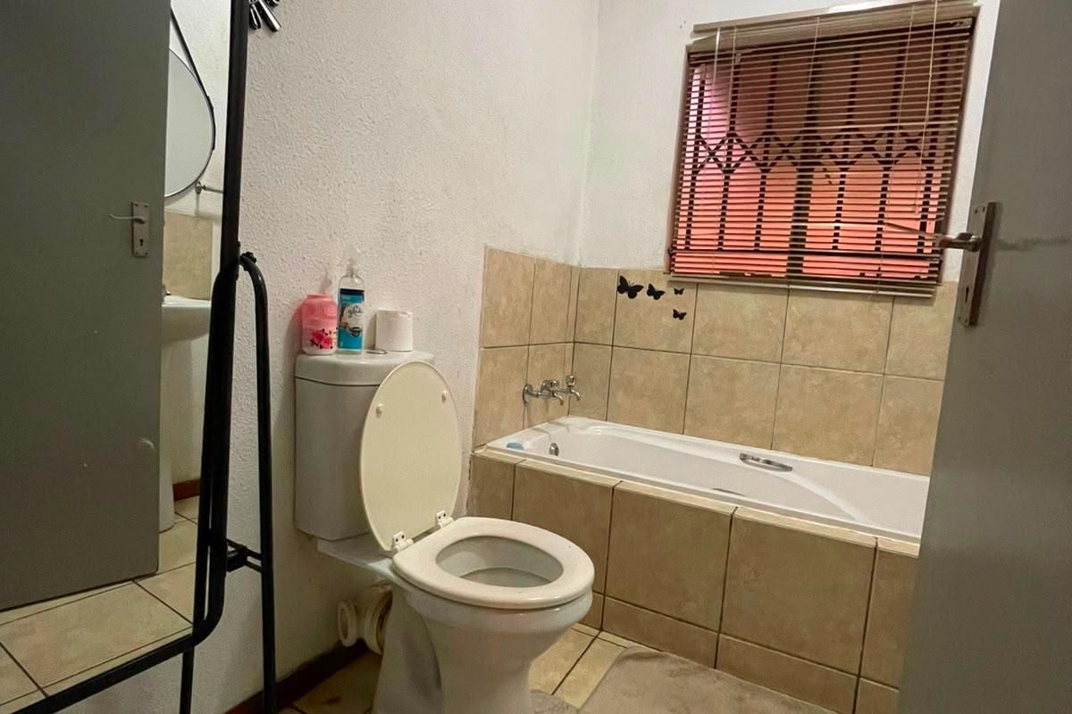 A functional bathroom featuring a bathtub, toilet, and tiled finishes, equipped with a security gate on the window for added safety.