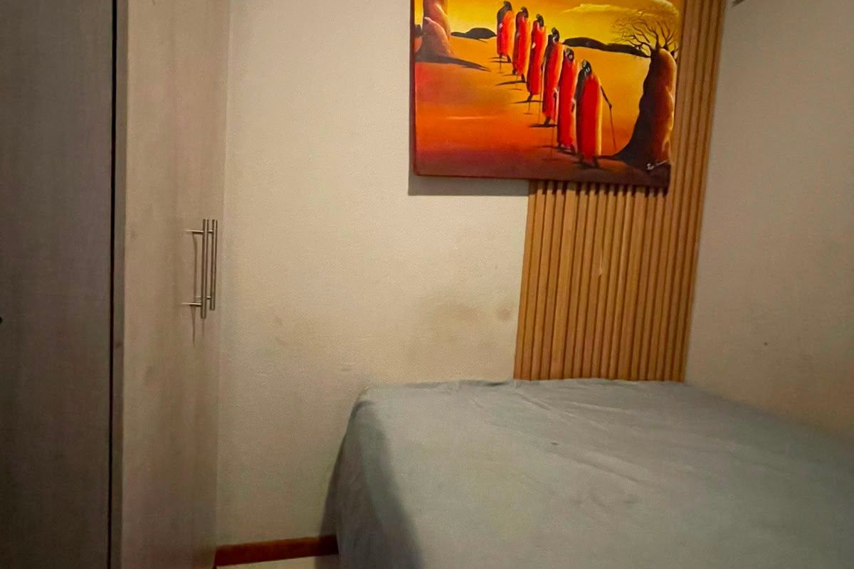 A compact bedroom featuring built-in cupboards, a timber slat wall accent, and a wall-mounted air conditioning unit.
