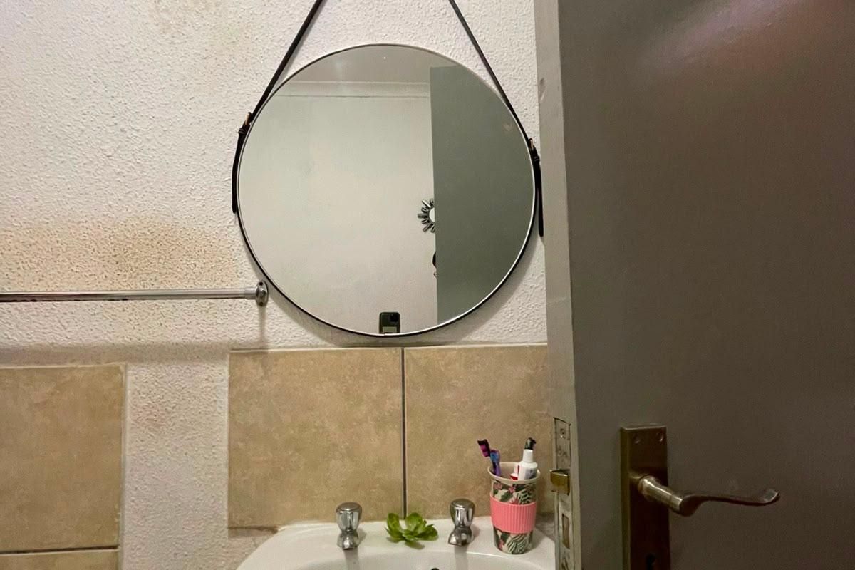 A compact bathroom featuring a pedestal basin with chrome taps and tiled splashback, showing signs of wall surface wear and water staining.