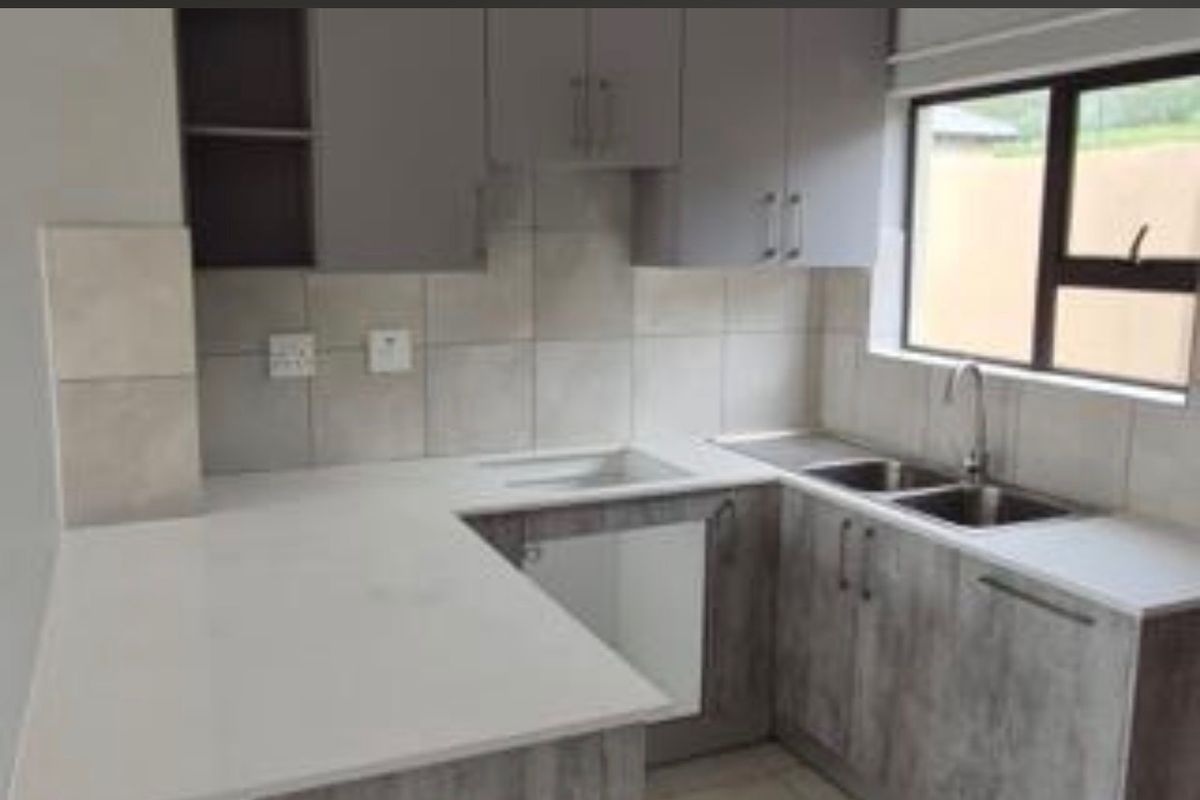 A modern kitchen featuring grey laminate cabinetry, stone countertops, a double bowl stainless steel sink, and a tiled splashback.