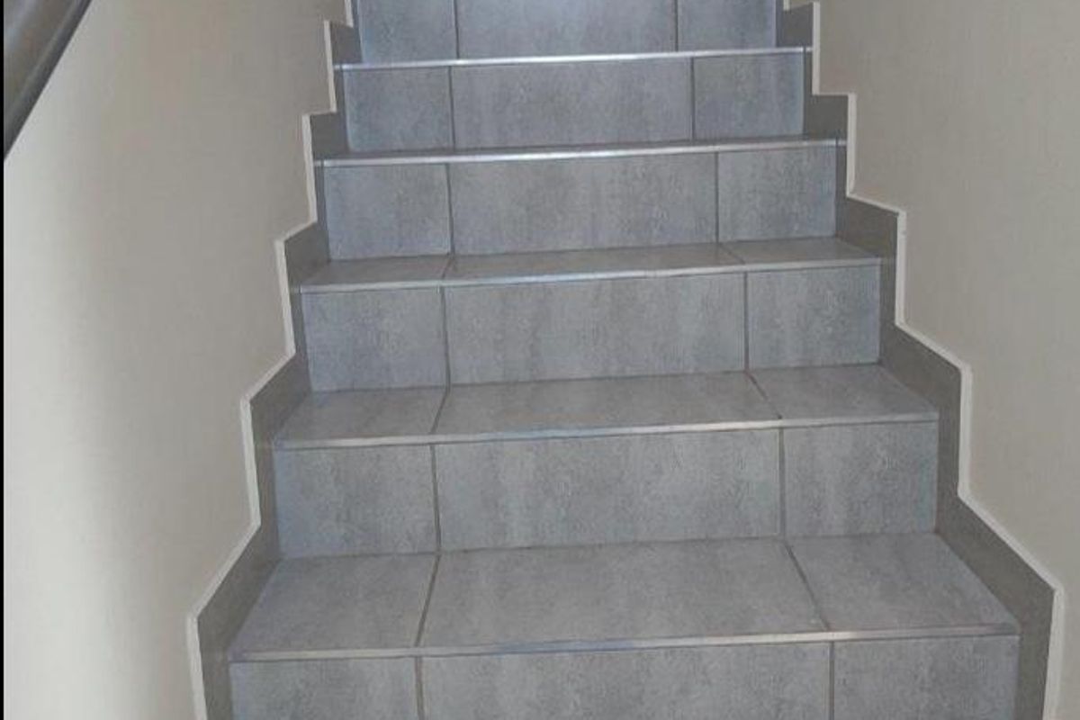 A clean, modern staircase featuring grey ceramic tiles and a sturdy metal handrail, providing access between levels in the townhouse.