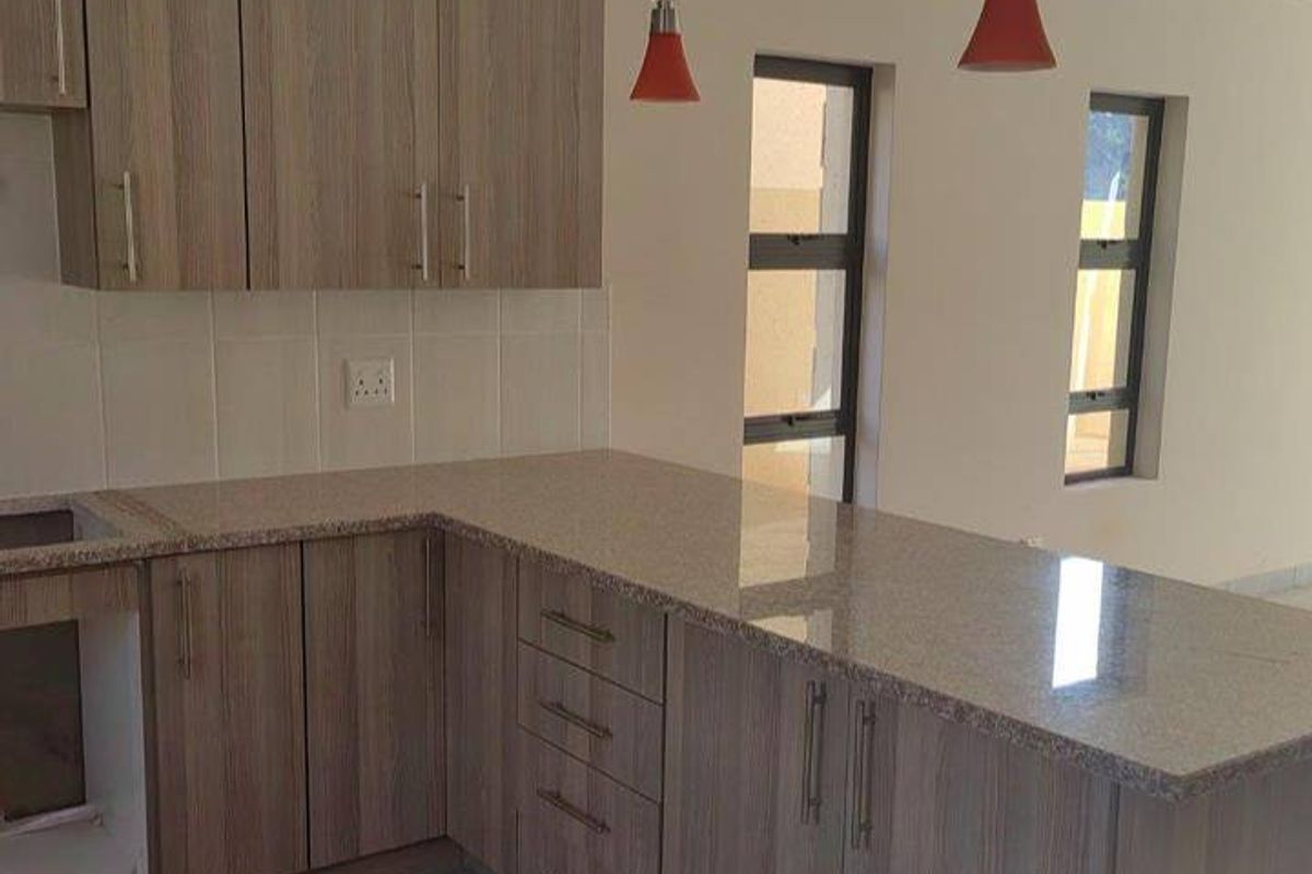 A modern kitchen featuring wood-finish cabinetry, granite countertops, and tiled flooring, currently awaiting the installation of built-in appliances.