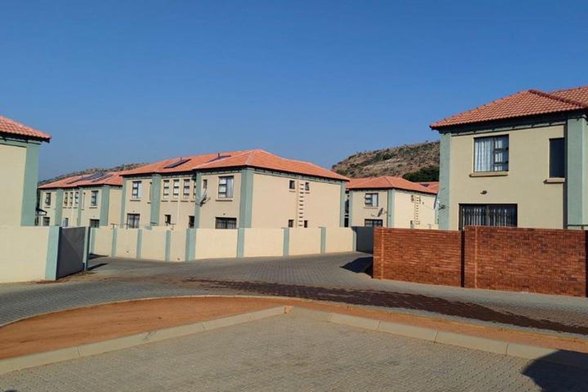 A view of the townhouse complex exterior featuring paved driveways, brick boundary walls, and tiled roof structures.
