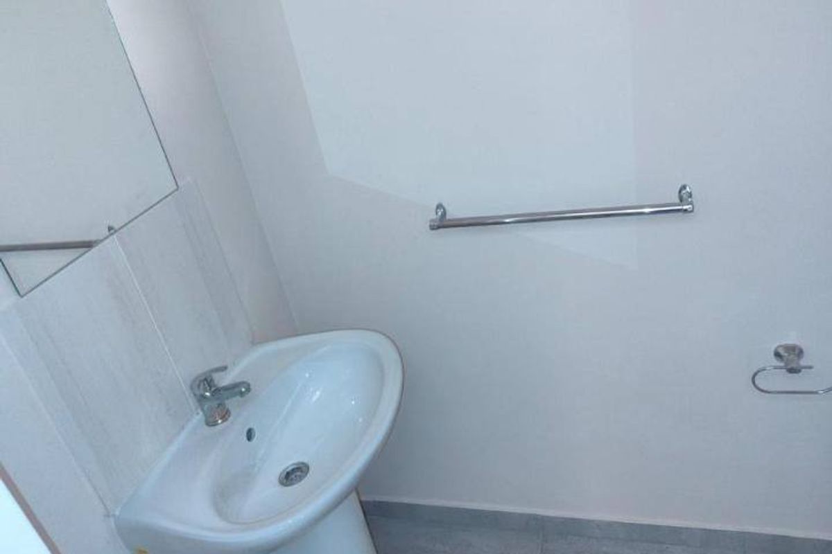 A clean, minimalist bathroom featuring a white pedestal basin, chrome fixtures, and a wall-mounted mirror.