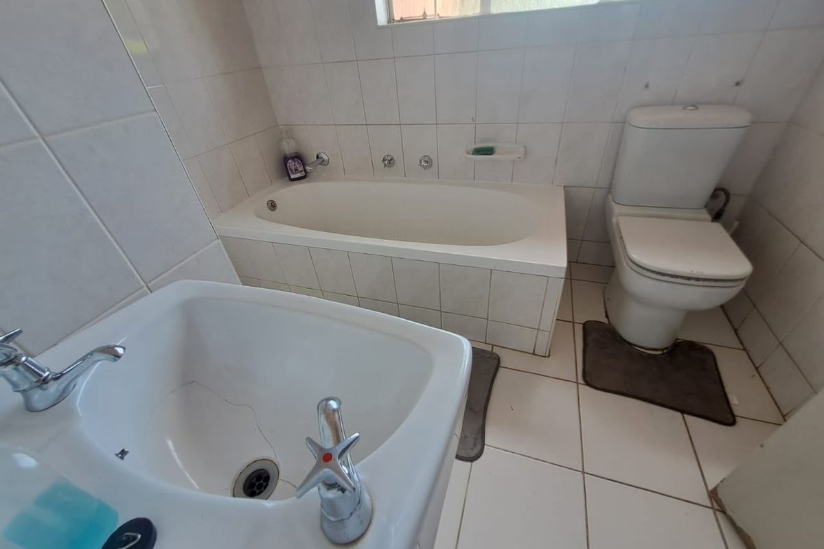 A dated bathroom featuring a built-in bathtub, pedestal basin, and toilet with white ceramic wall and floor tiling.