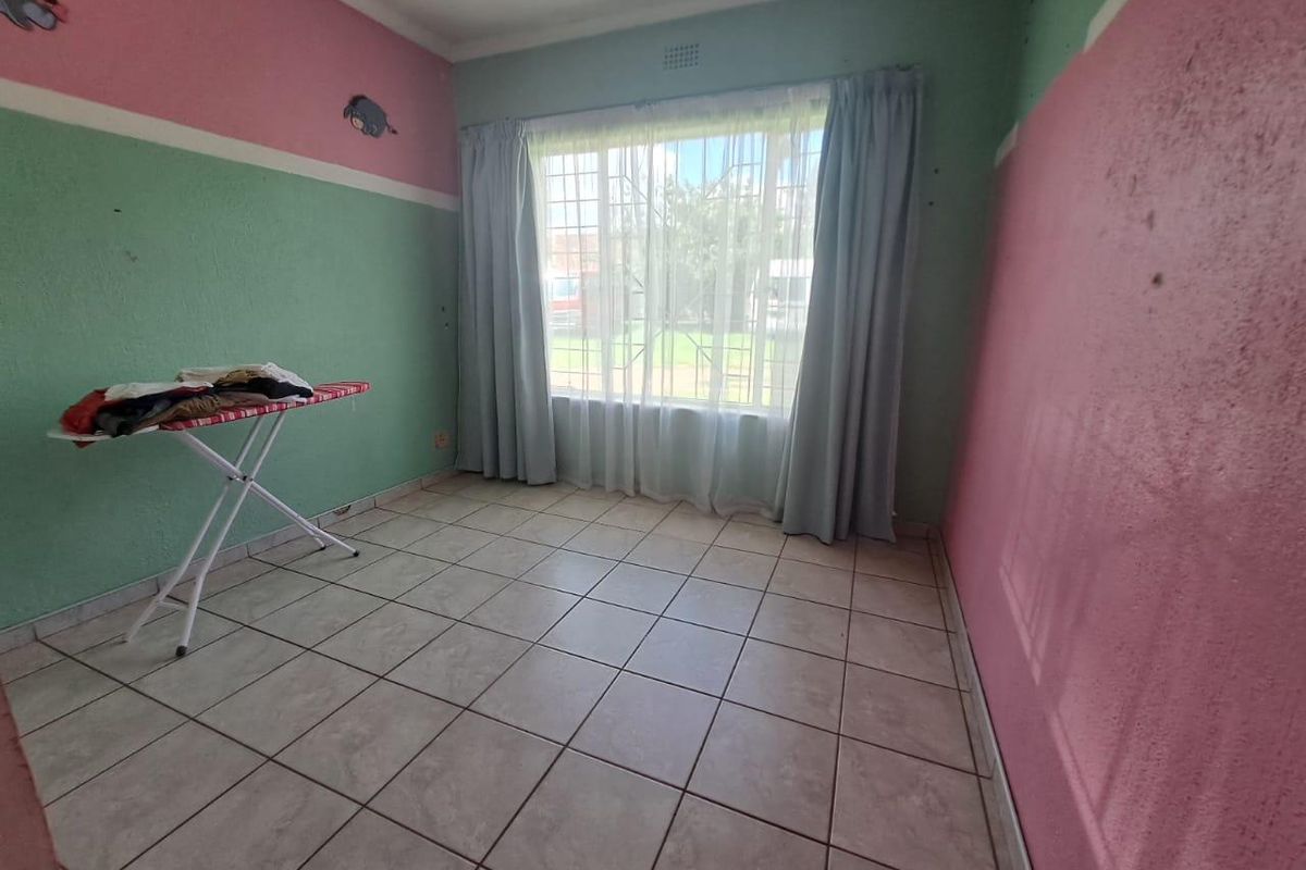 A vacant bedroom featuring tiled flooring and security bars on the window, requiring cosmetic updates to the wall finishes.