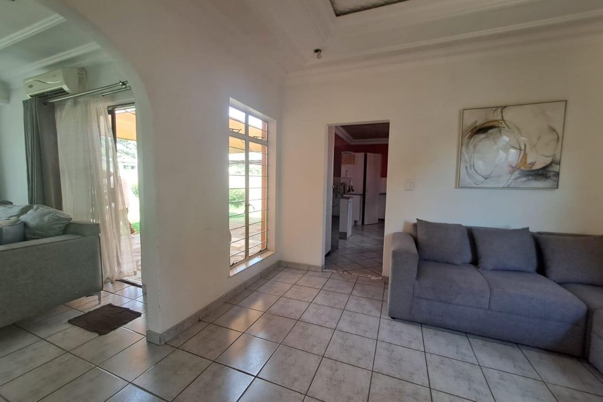 A living room featuring tiled flooring, a recessed ceiling, and an archway leading to an adjacent space with access to the exterior.