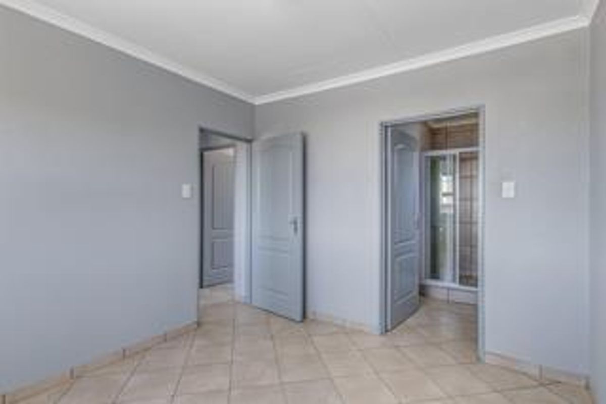 A clean, empty bedroom featuring neutral grey walls, tiled flooring, coved cornicing, and direct access to an en-suite bathroom.