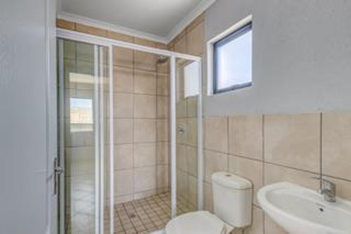 A clean and functional bathroom featuring a glass-enclosed shower, pedestal washbasin, and neutral ceramic wall tiling.