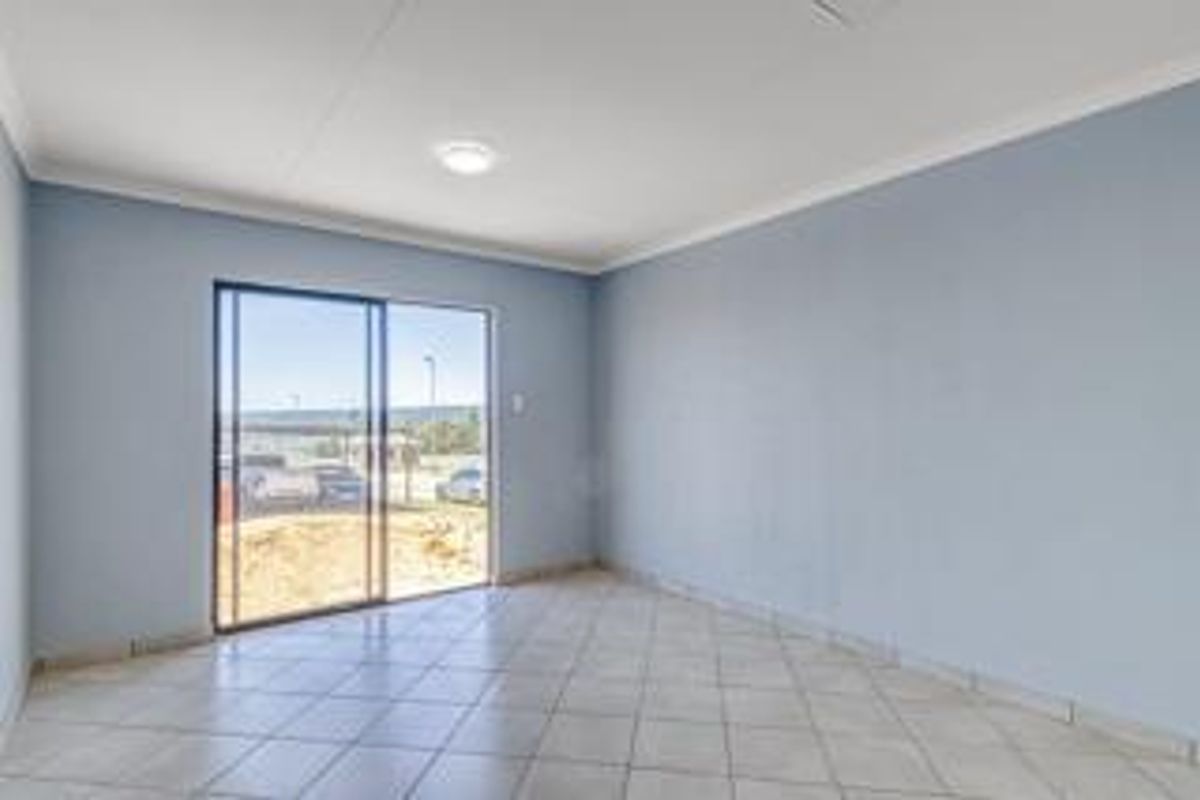 A bright and spacious empty living area featuring neutral tiled flooring and a large sliding glass door providing natural light and outdoor access.