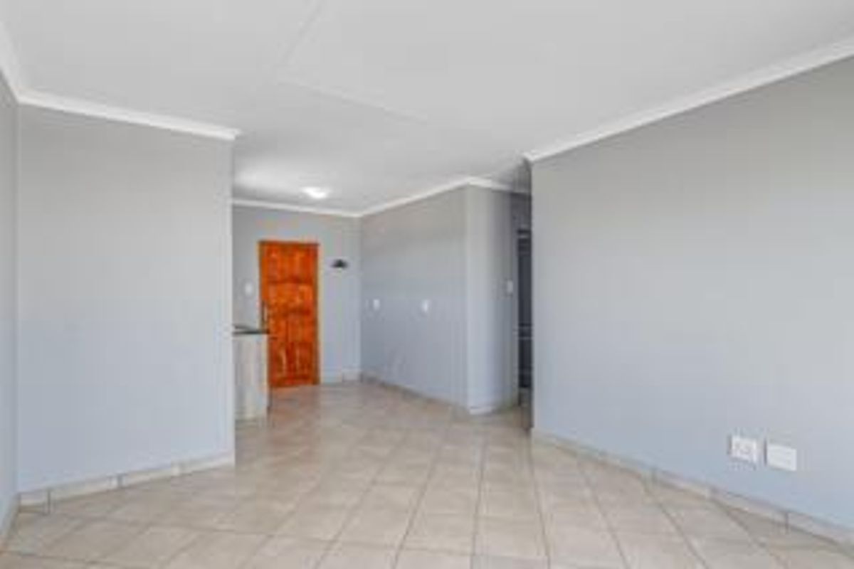 An empty, open-plan living area featuring neutral grey walls, tiled flooring, and a wooden entrance door.